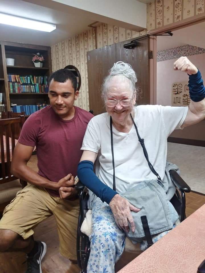A man in a maroon t-shirt and a woman wearing glasses flex their arms together for a portrait