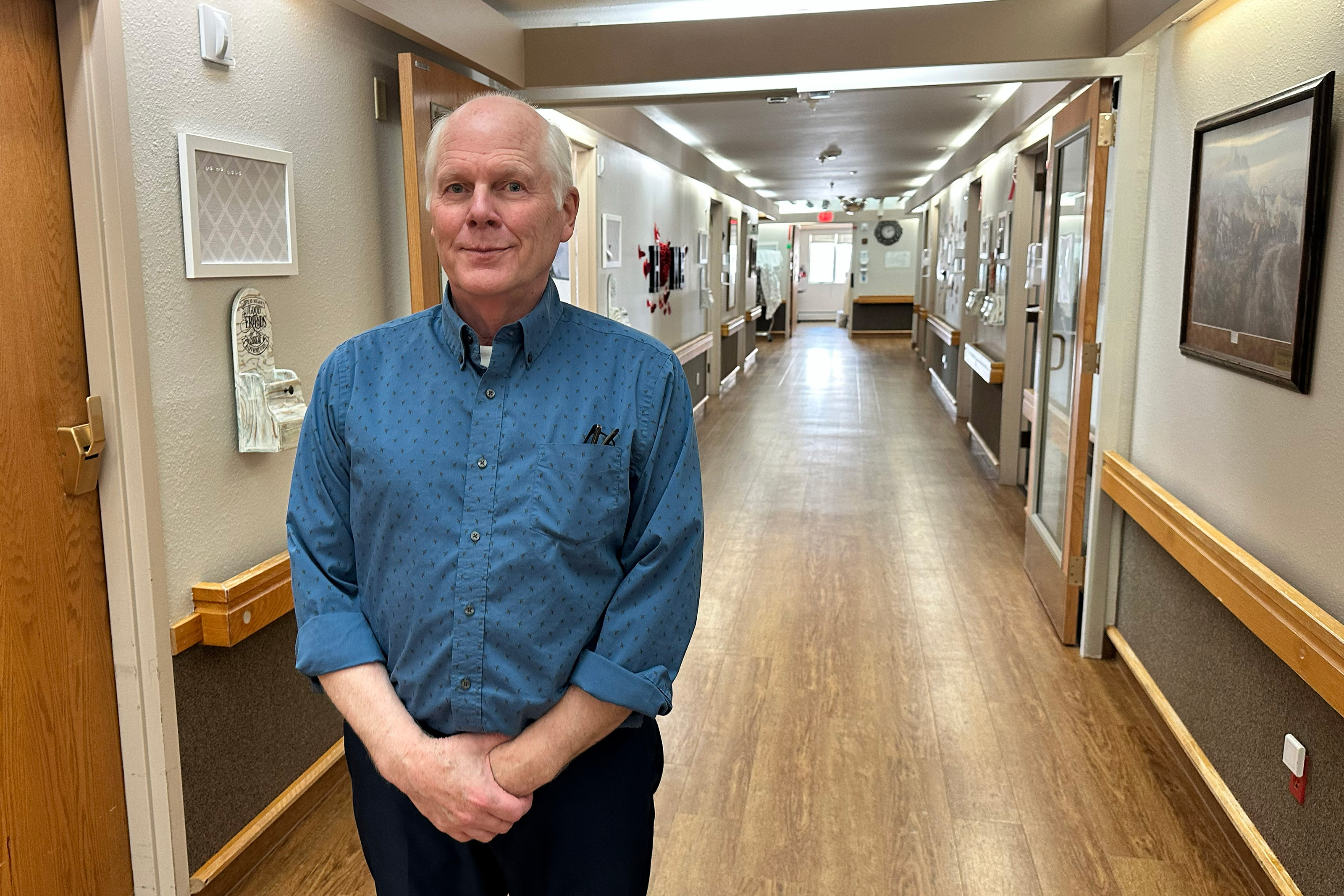 A man in a blue button-down shirt stands in a hospital hallway.