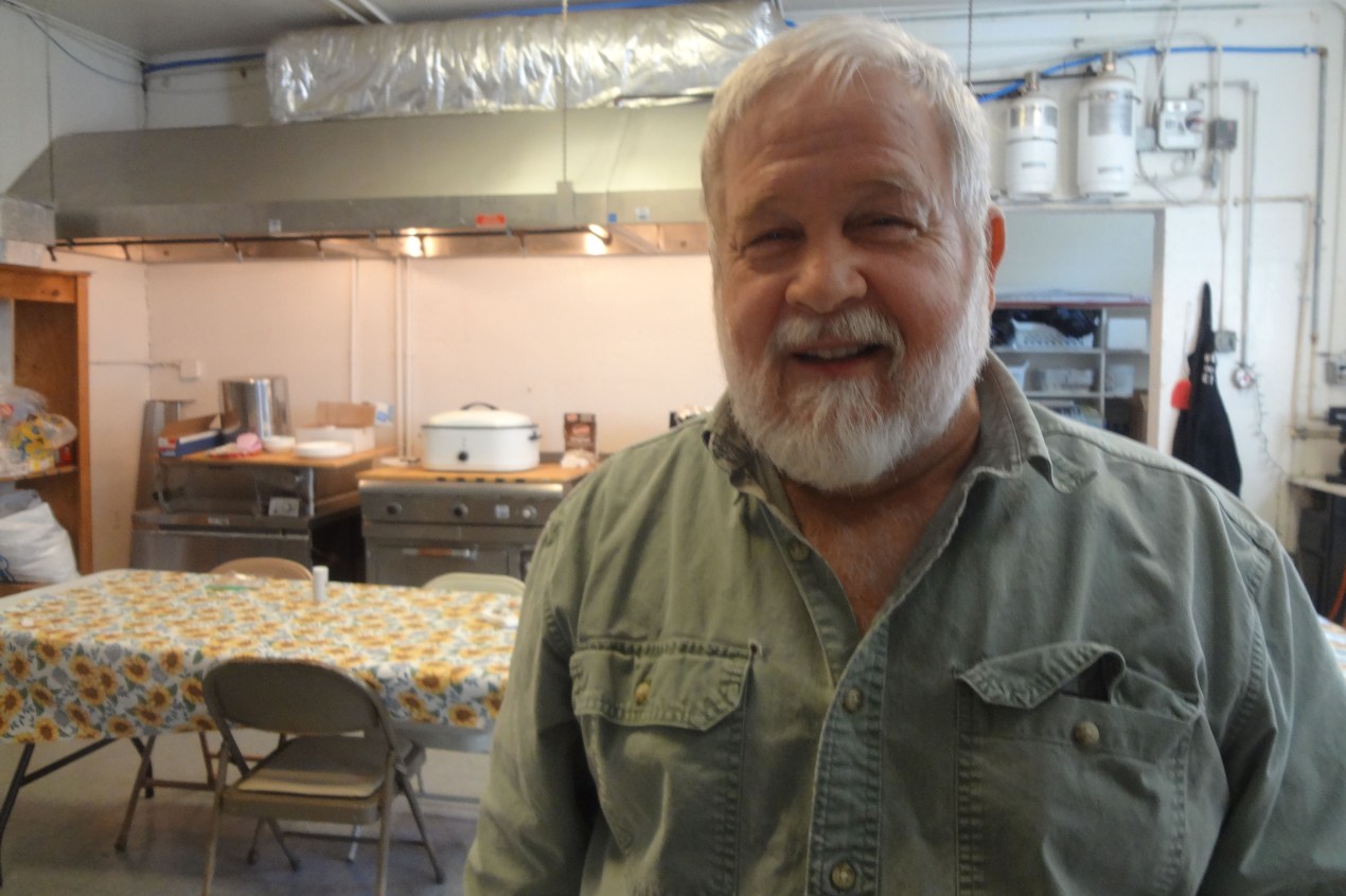 An older man with white hair and beard smiles at the camera.