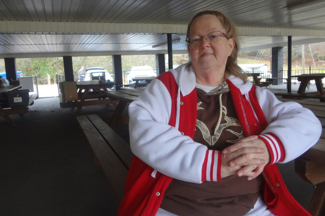An older woman wearing a white and red sports jacket sits comfortably for a photo.