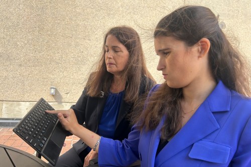 The mother of an adult daughter holds a keyboard, which her daughter touches with her finger.