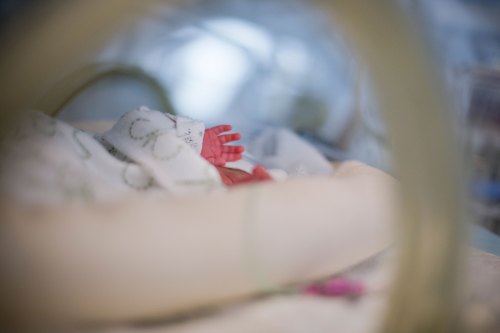 An unidentifiable baby lies in an incubator in a NICU and holds their right hand near their head.