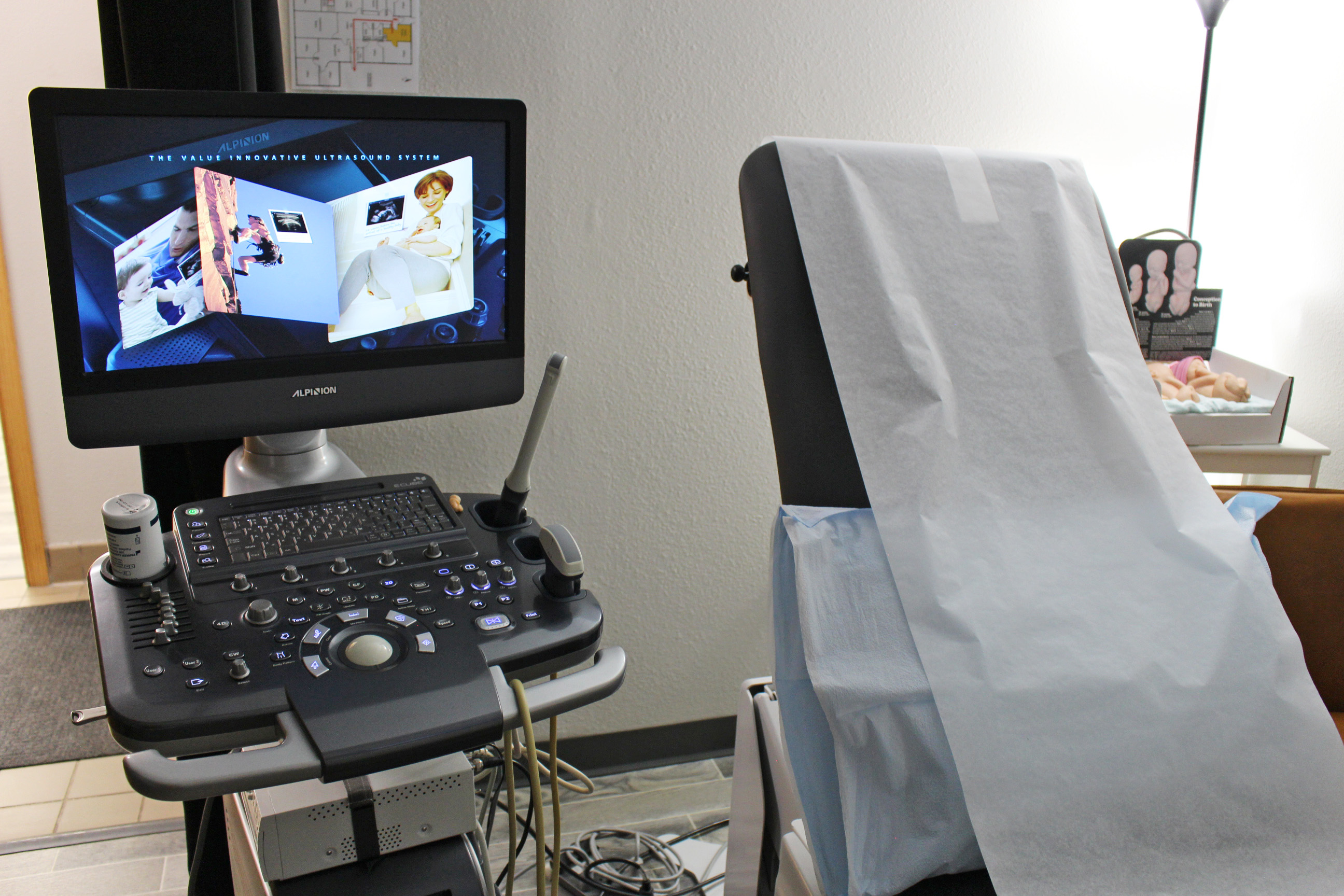 An exam table lined with paper is next to an ultrasound machine and computer monitor.