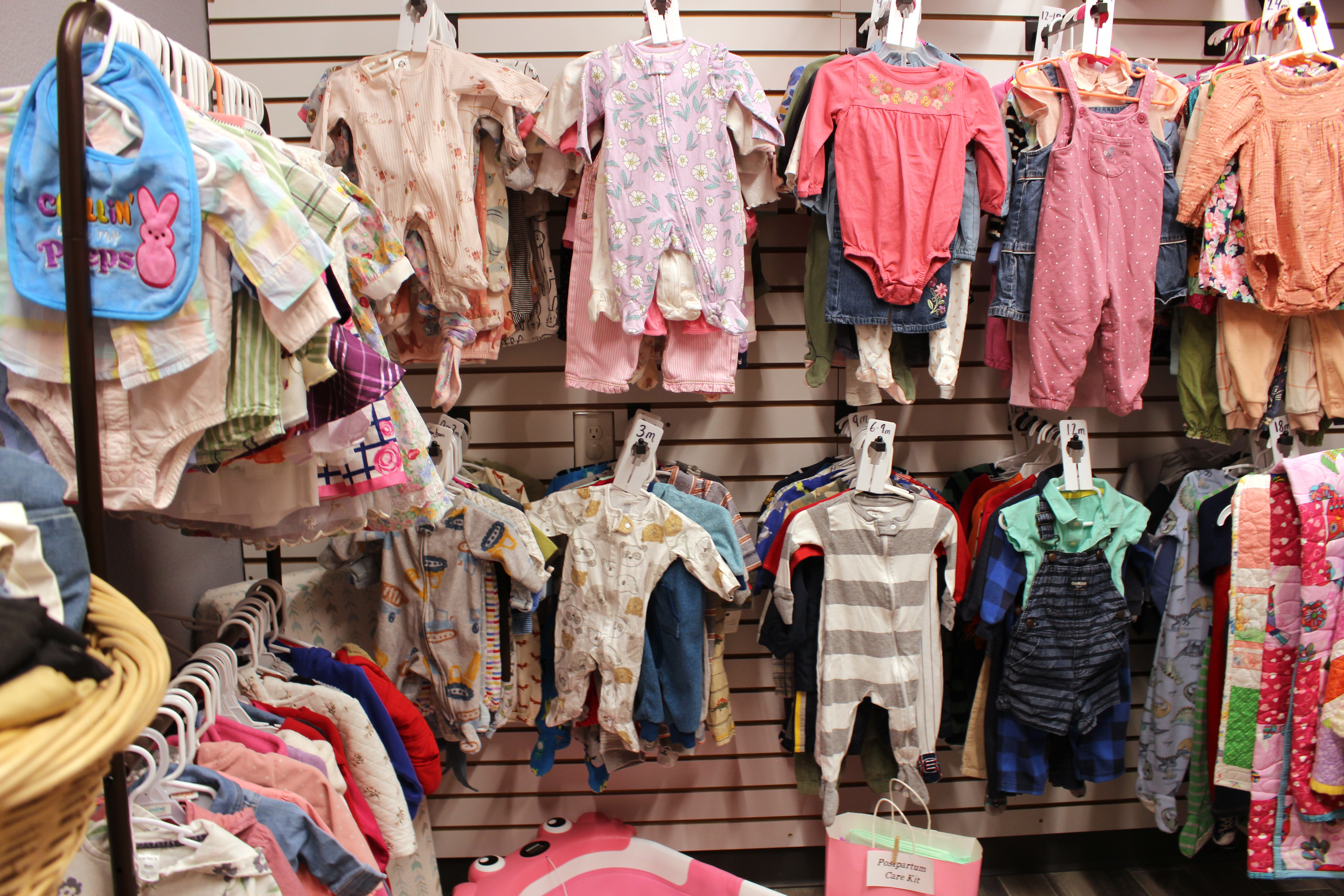 A variety of baby clothes in various colors are hung on display racks.