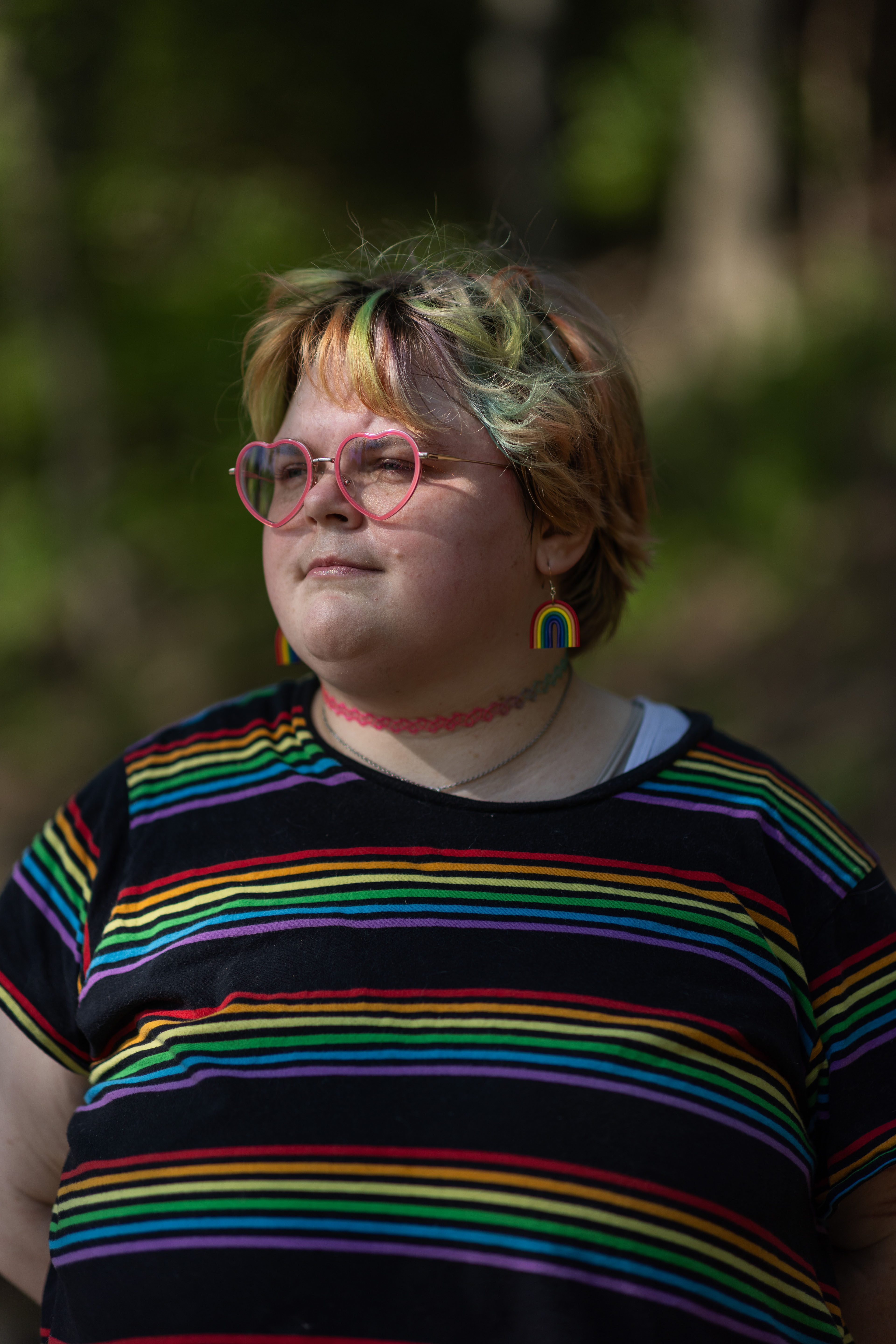 A portrait of a young person wearing a rainbow T-shirt and heart-shaped glasses.