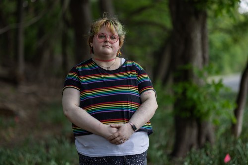 A portrait of a young person wearing a rainbow T-shirt and heart-shaped glasses.