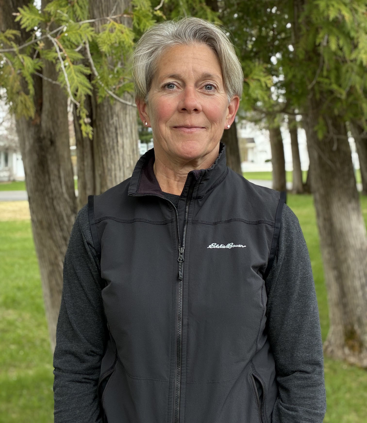 A woman with very short gray hair wearing a black fleece jacket smiles in the direction of the camera.
