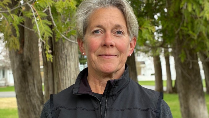 A woman with very short gray hair wearing a black fleece jacket smiles in the direction of the camera.