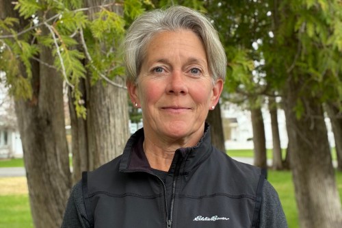 A woman with very short gray hair wearing a black fleece jacket smiles in the direction of the camera.