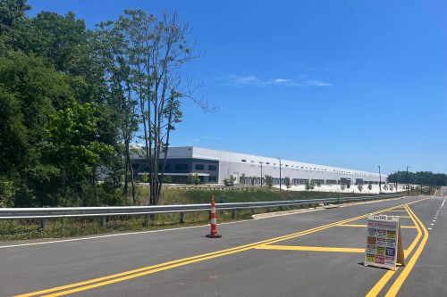 A massive warehouse is visible on the far side of a highway.