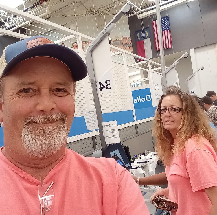 A man takes a selfie, smiling. His sister is behind him.