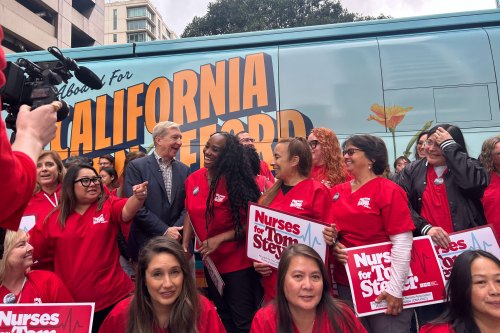 A group of people — most wearing red shirts — mingle in front of a bus with the words "All Aboard For A California You Can Afford" on its side.