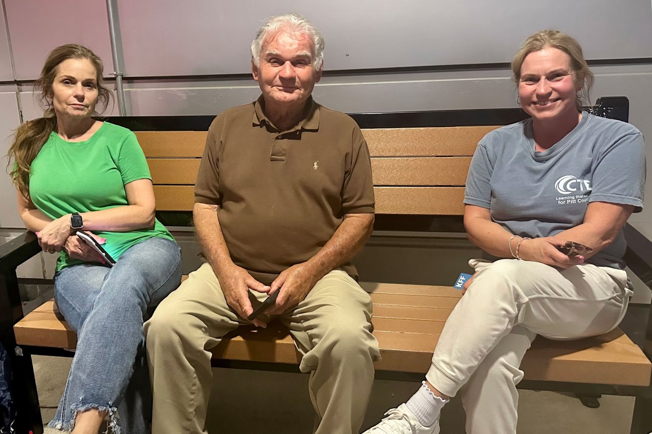 Two women sit on a bench outside. A man sits between them.