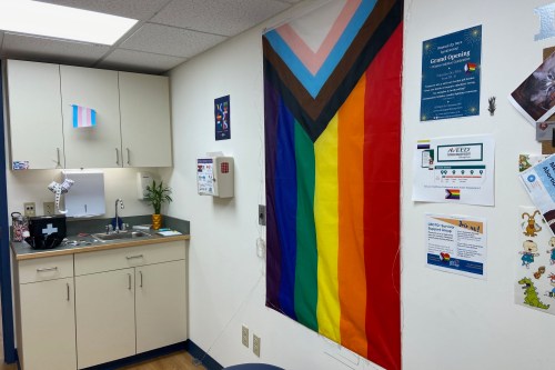An interior photo of a doctor's office. A large LGBTQIA+ flag hangs on the wall.