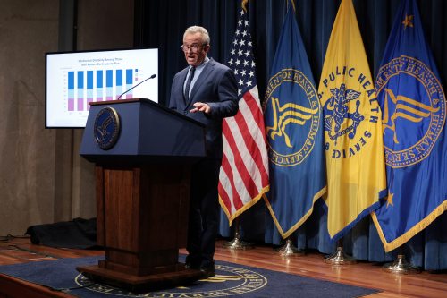 A photo of Robert F. Kennedy Jr. at a podium at the Department of Health and Human Services. A screen to the side of him shows a chart titled, "Intellectual Disability Among Those with Autism Continues to Rise."