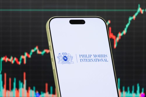 A smartphone displays the logo of Philip Morris International Inc. in front of a screen showing the company's latest stock market chart, which has increased in value.