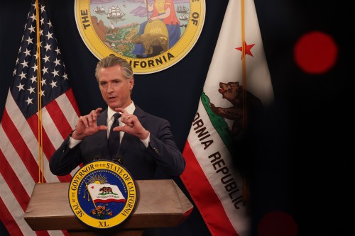 Gavin Newsom speaks behind a podium at a press conference. The American flag and California flag are behind him.