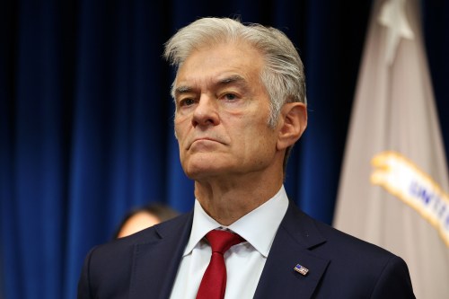 A senior man with grey hair wearing a navy suit and red tie