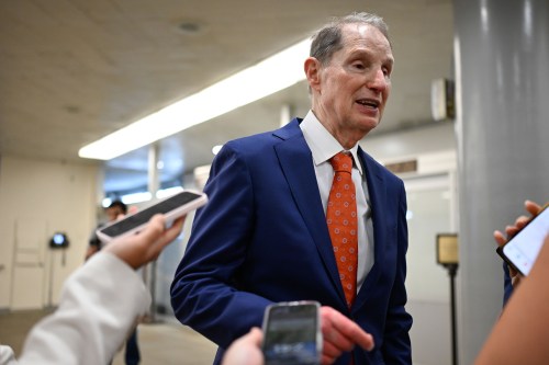 Senator Ron Wyden walks past a few reporters, who hold up their cell phones as recording devices as he speaks in passing.