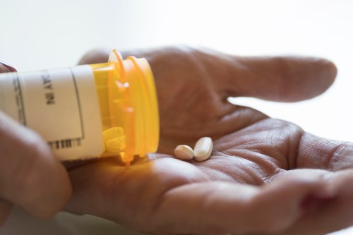 A close-up shot of a hand holding two pills that have been dropped out of an orange pill bottle.