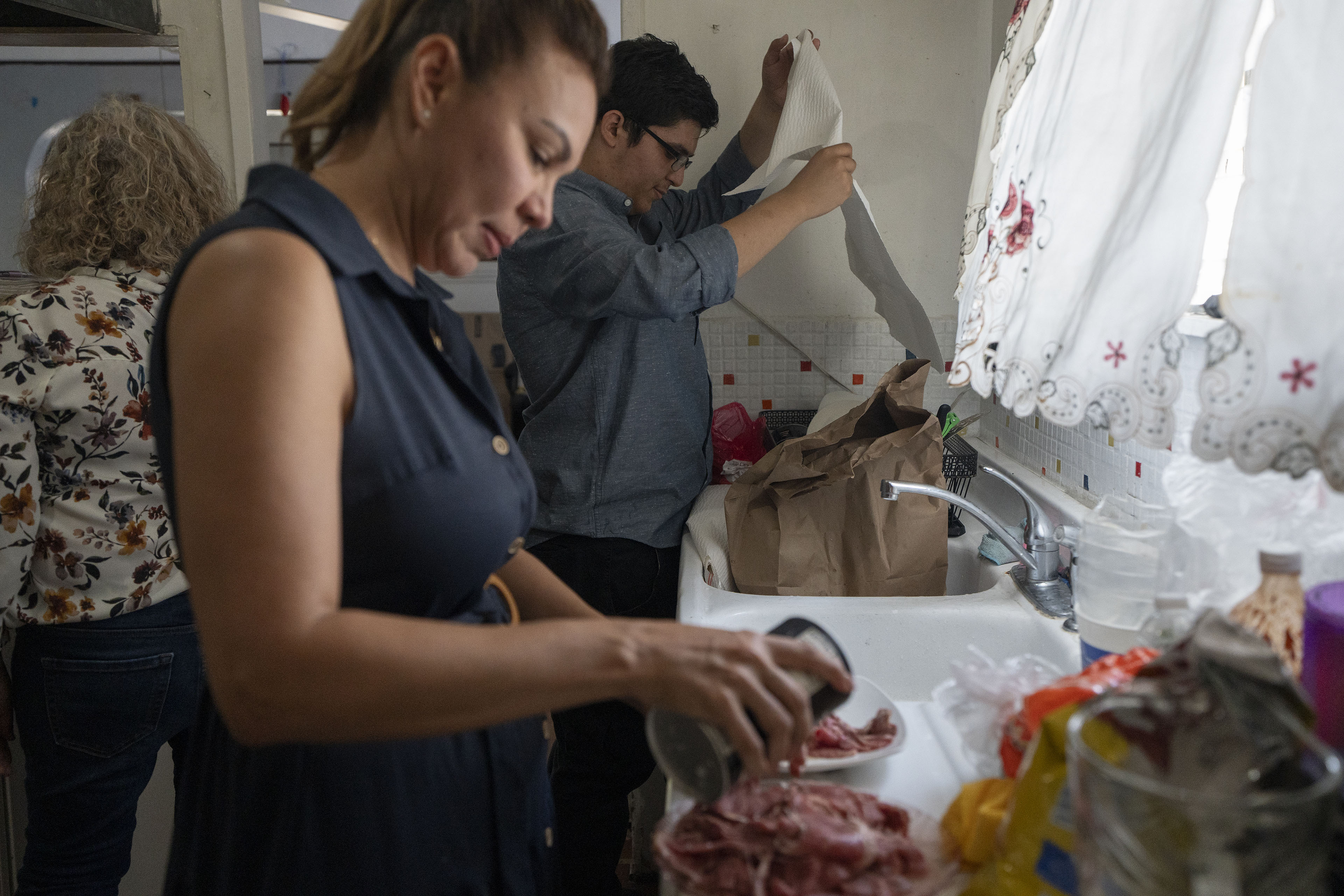 A man and woman stand in front of a sink and an open window as they prepare food in a kitchen