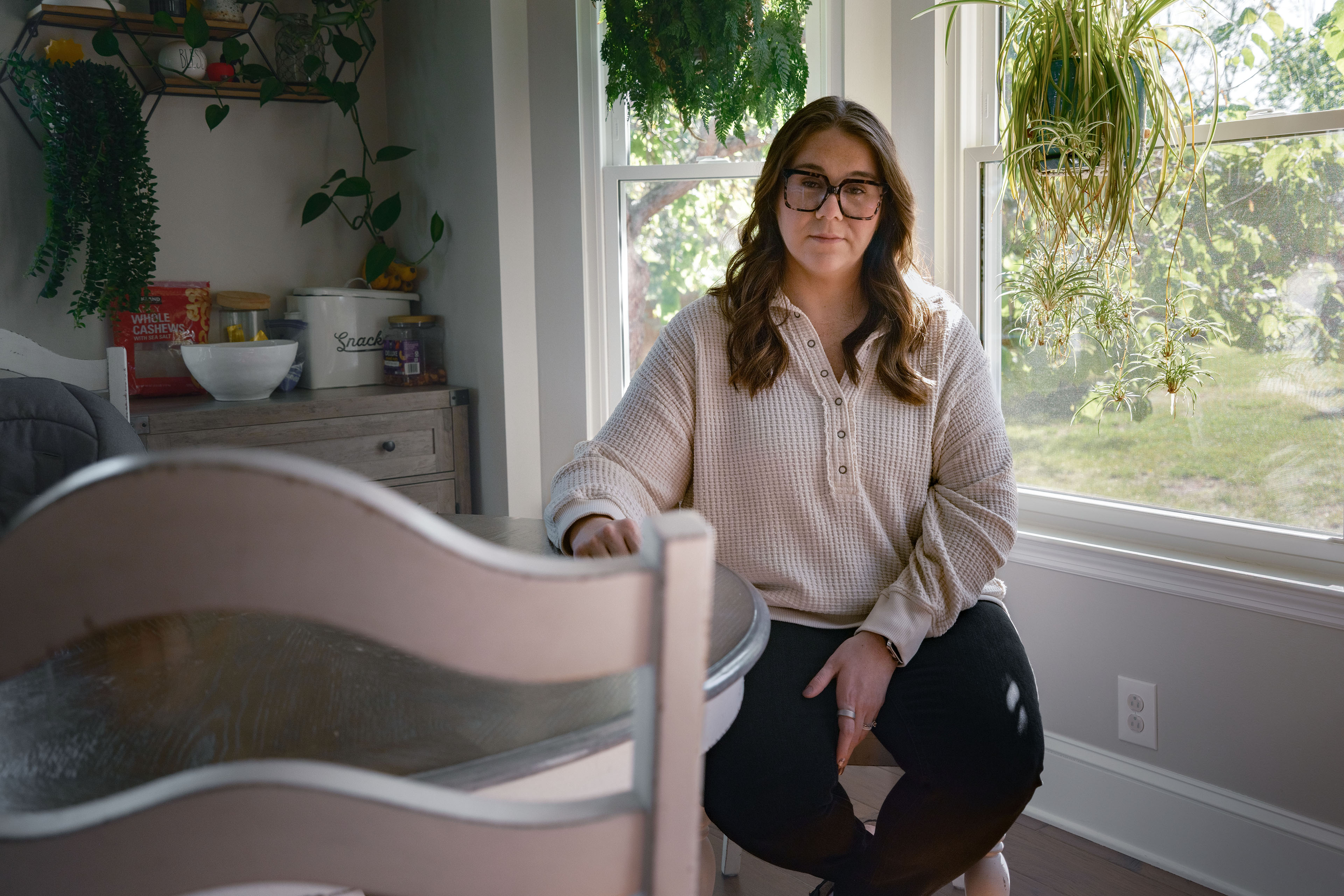 A woman wearing casual clothing sits in her sunlit dining room.