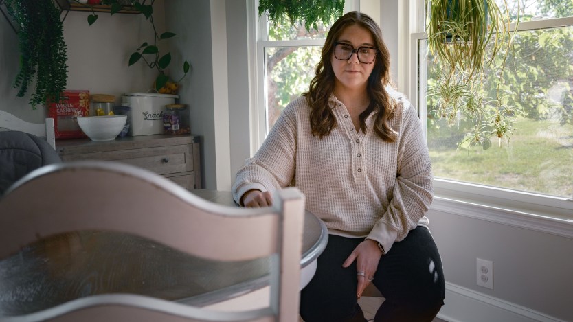 A woman wearing casual clothing sits in her sunlit dining room.