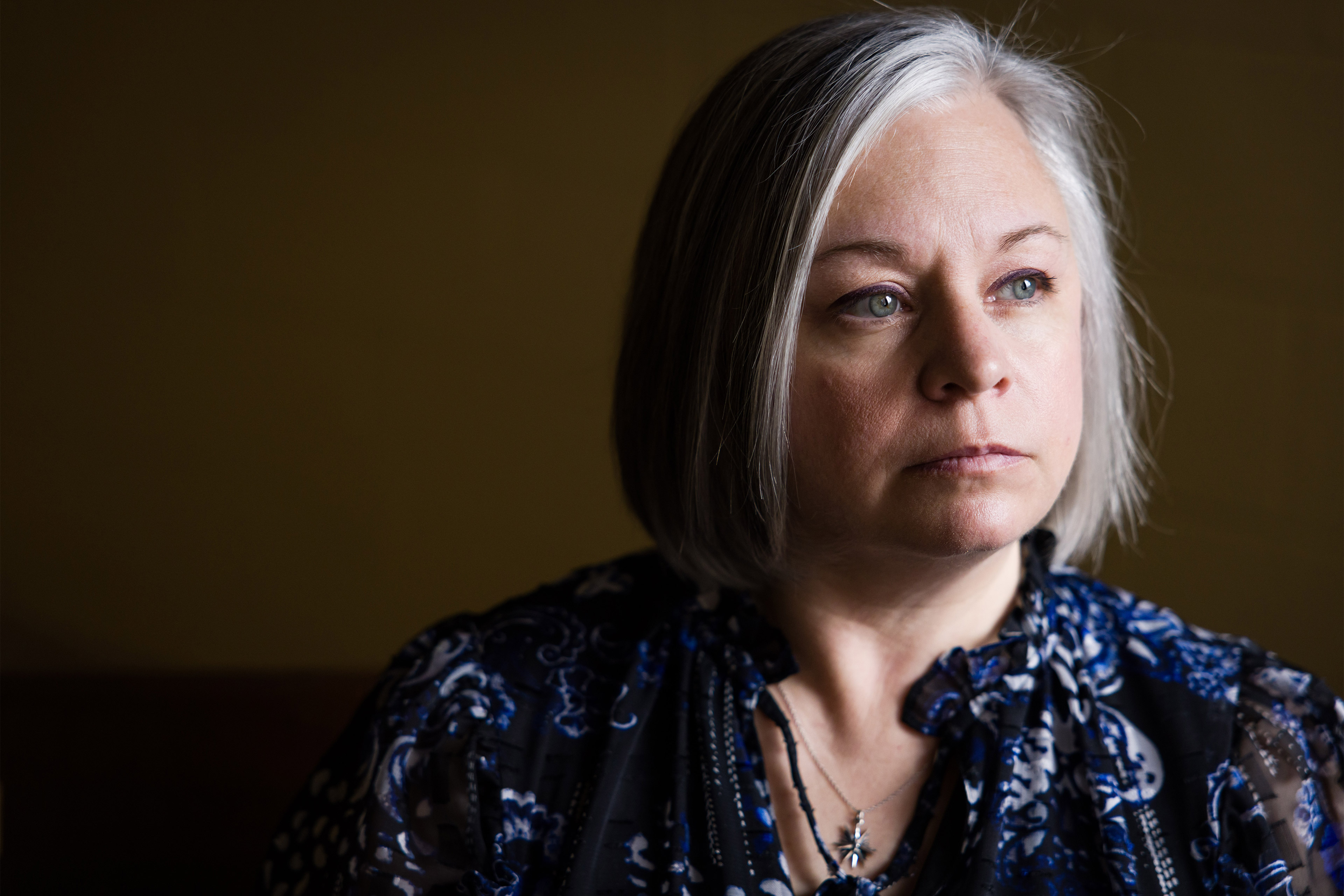 A portrait of a woman standing near a window or light source, casting dramatic shadows on half of her face.