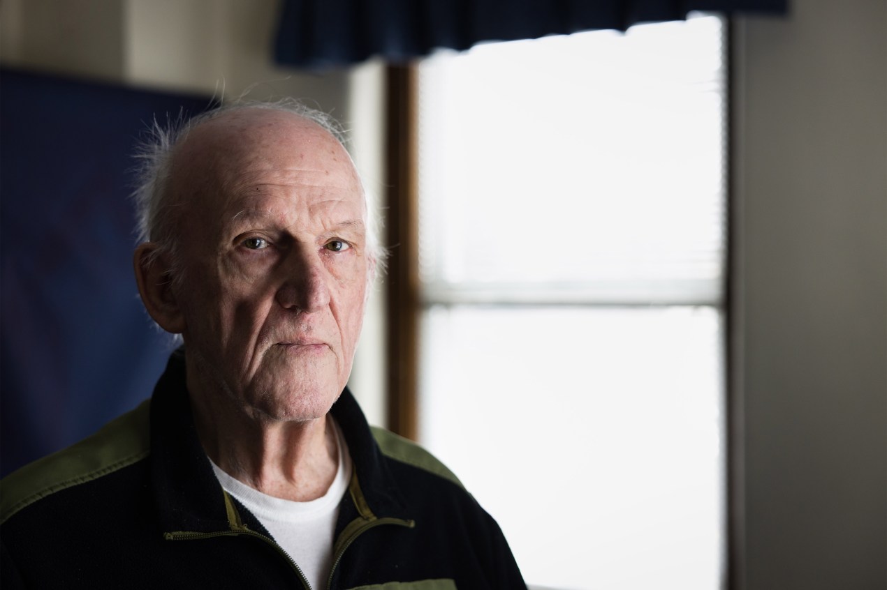 A man stands in front of  a window, casting harsh light on the right side of his face.