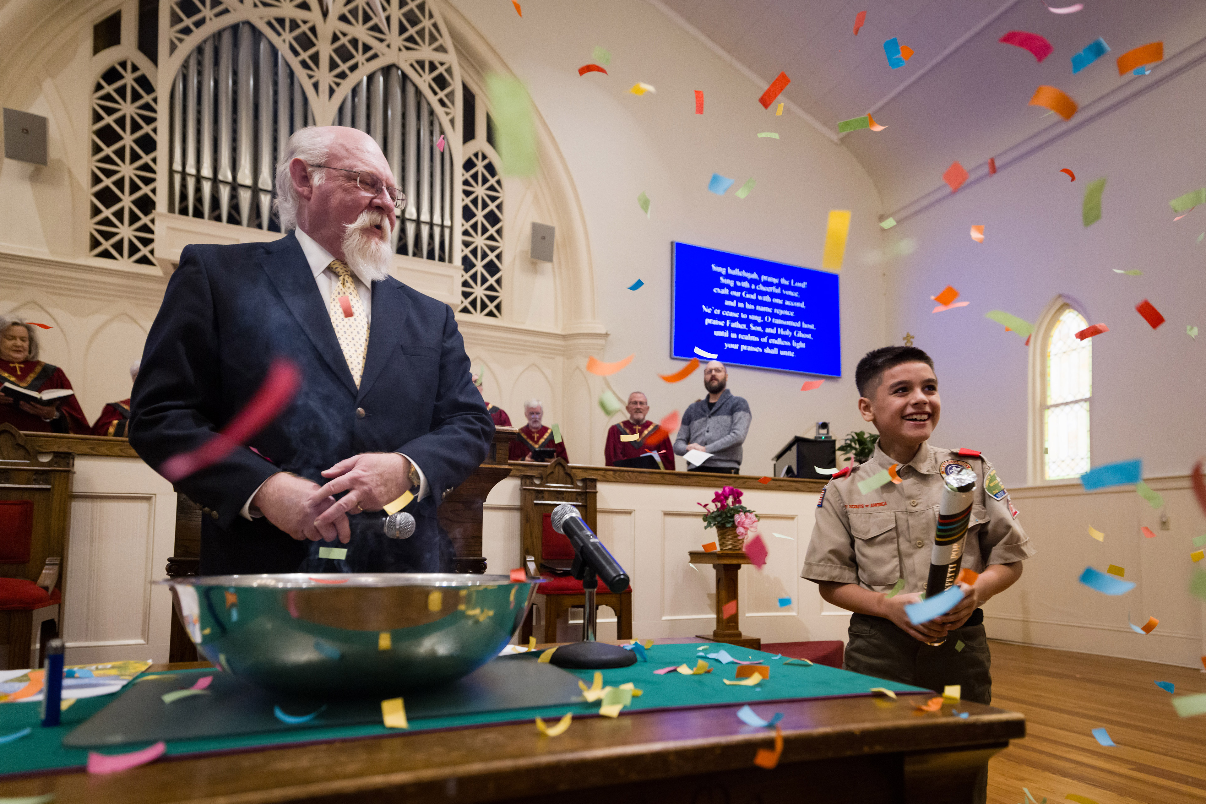 A young boy scout pops a confetti popper, sending multicolor confetti flying.