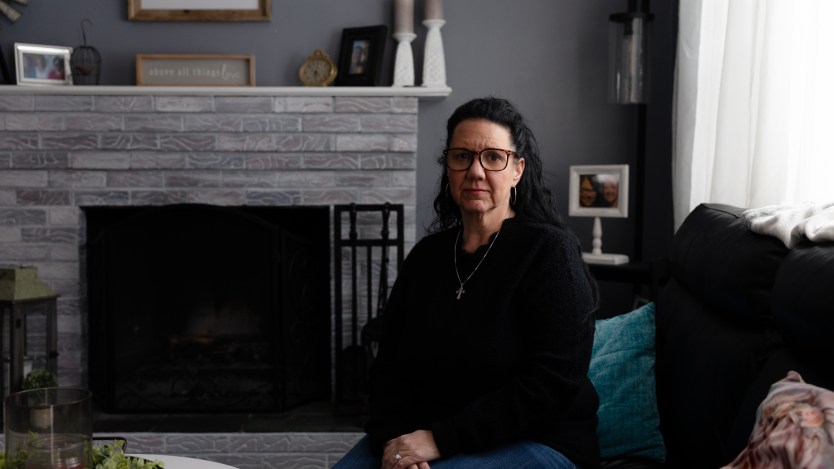 A woman sits on a couch in a living room and looks at the camera.