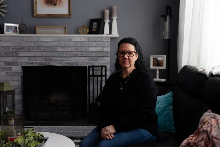 A woman sits on a couch in a living room and looks at the camera.