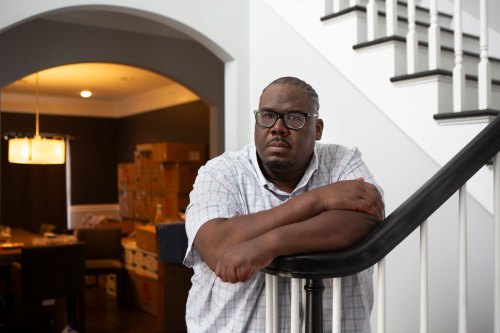 A man leans against a stair banister inside his home.