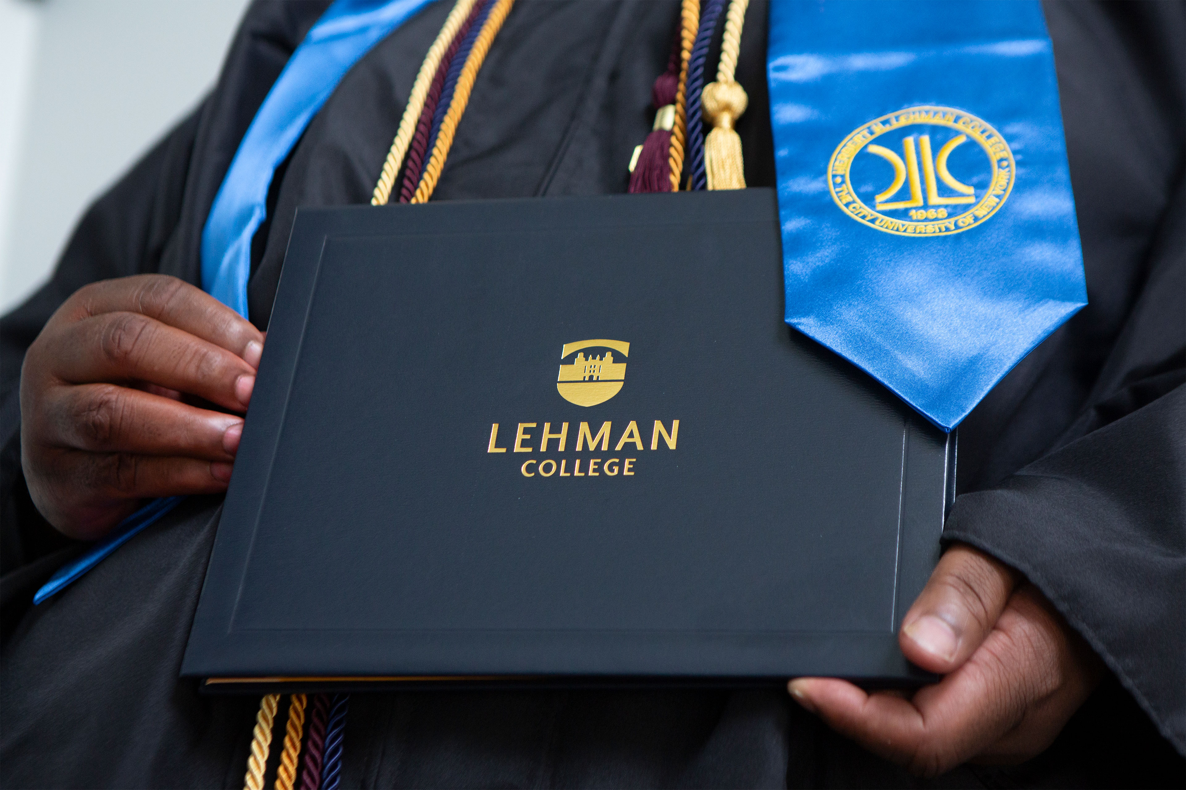 A man holds a diploma case with the logo of Lehman College on it.