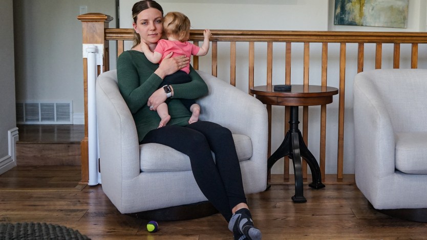 A mother sits in a living room chair, holding her baby.