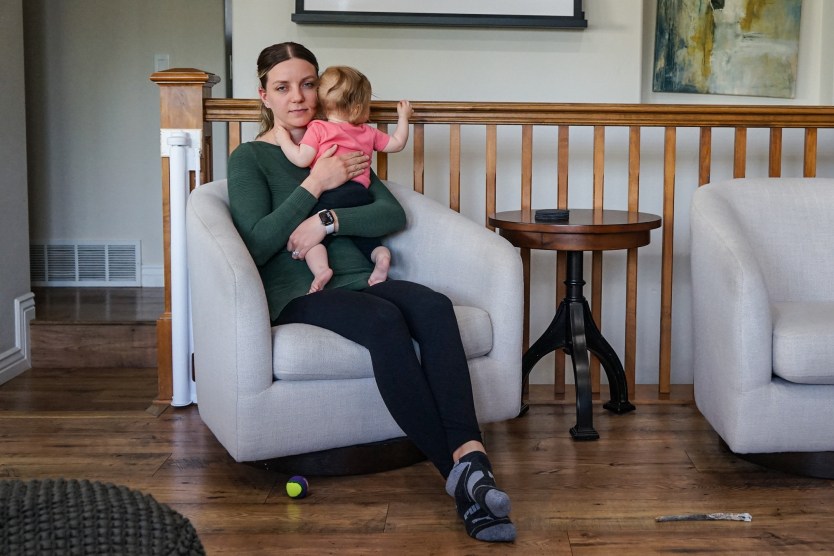 A mother sits in a living room chair, holding her baby.