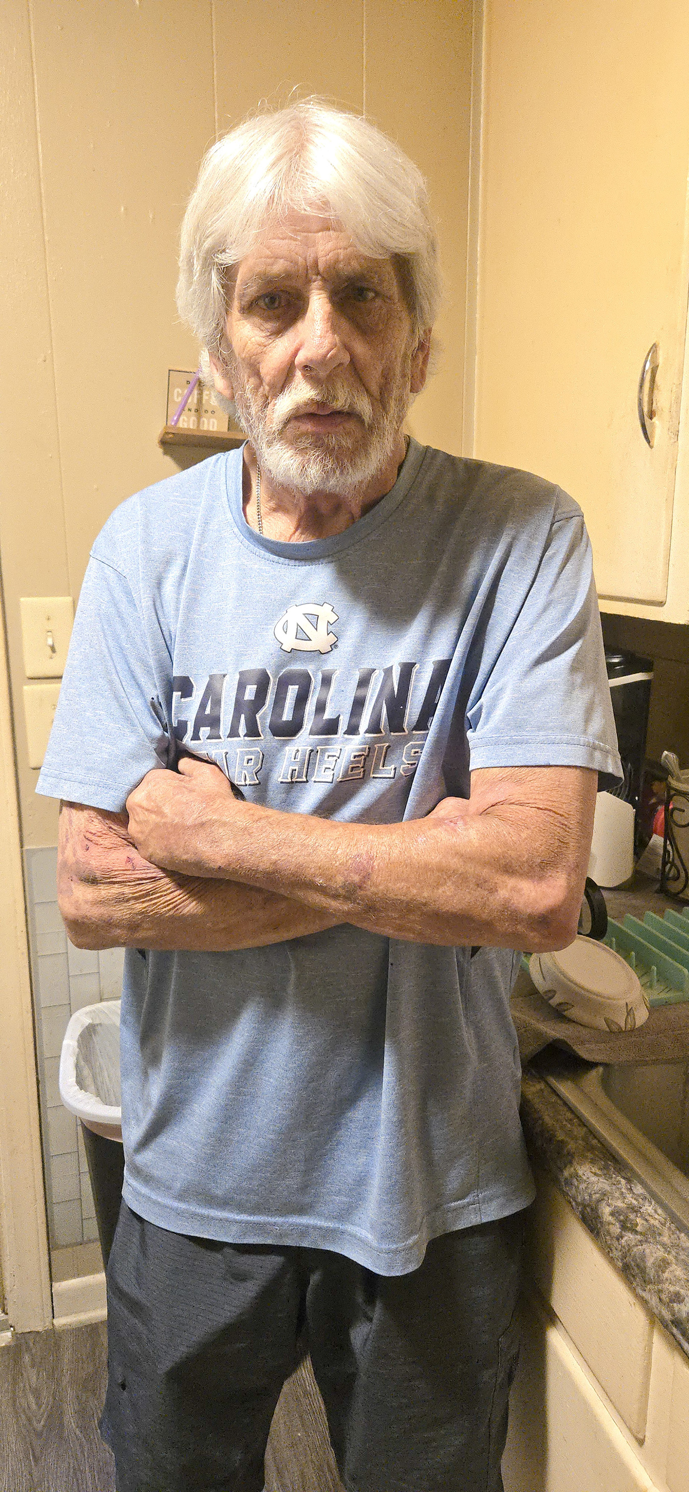 An older man with white hair stands with his arms crossed.