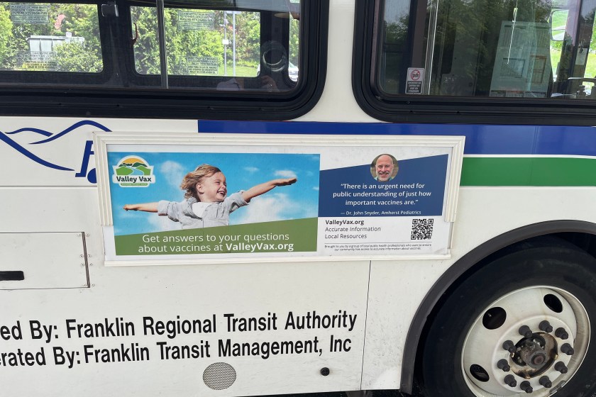 An advertisement on the outside of a public transit bus shows a child smiling with arms outstretched.