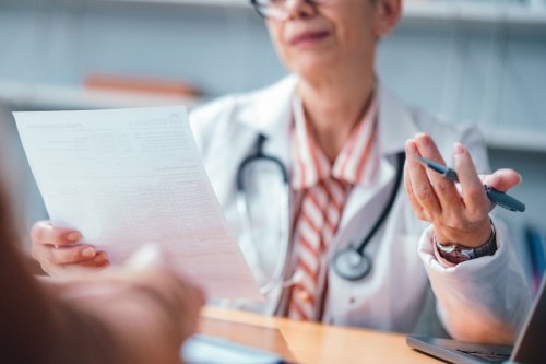 A doctor holding a document speaks with a patient who is out of frame.