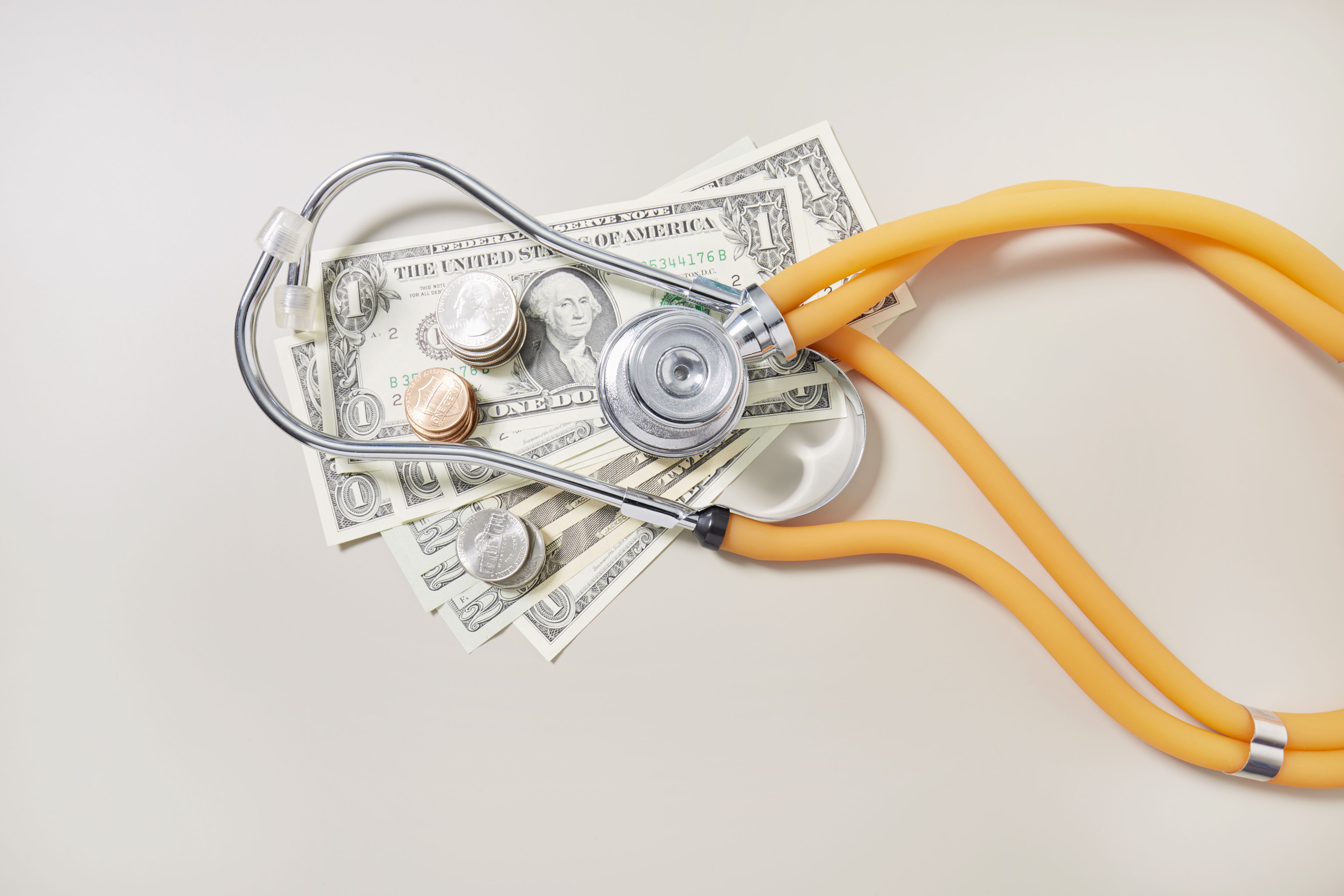A high angle view of American dollar bills and coins with a stethoscope resting on top of them.