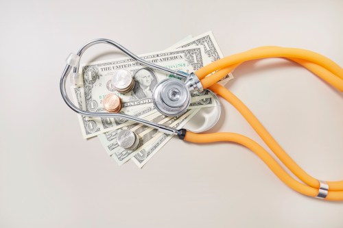 A high angle view of American dollar bills and coins with a stethoscope resting on top of them.