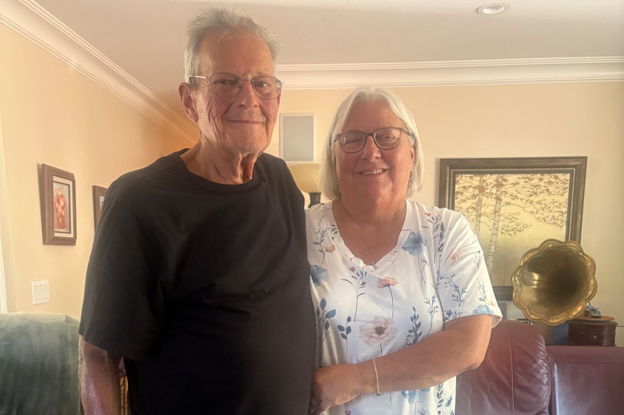 An older man and woman stand next to one another, smiling for a photo.