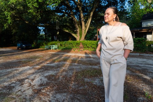 A Native American woman stands outside in the late afternoon sun.