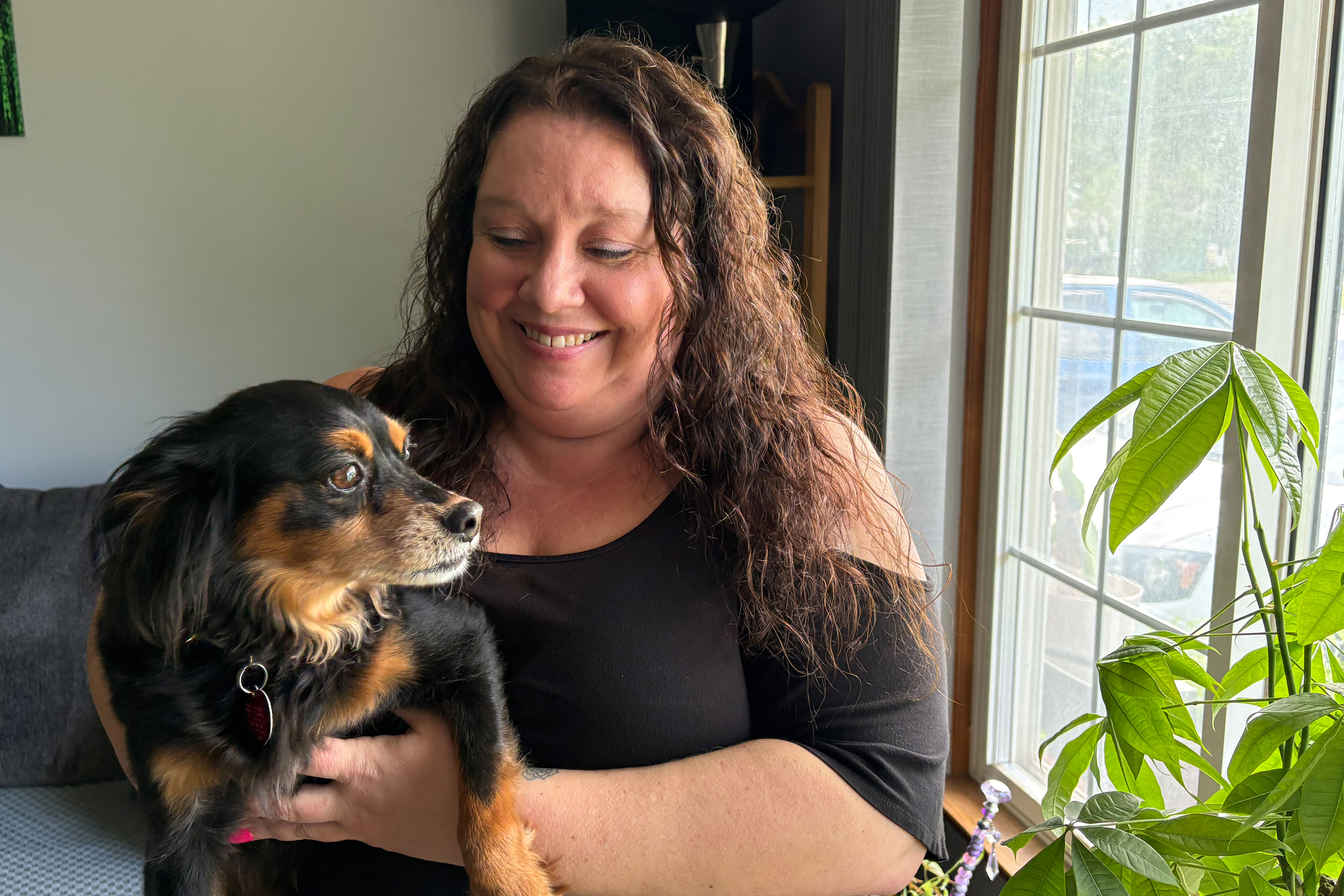 Marie Noon holds her dog as they stand by a window.