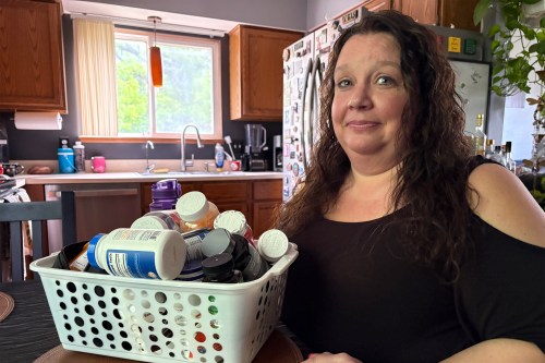 A woman sits at a kitchen table. On the table rests a caddy filled with several large pill bottles.