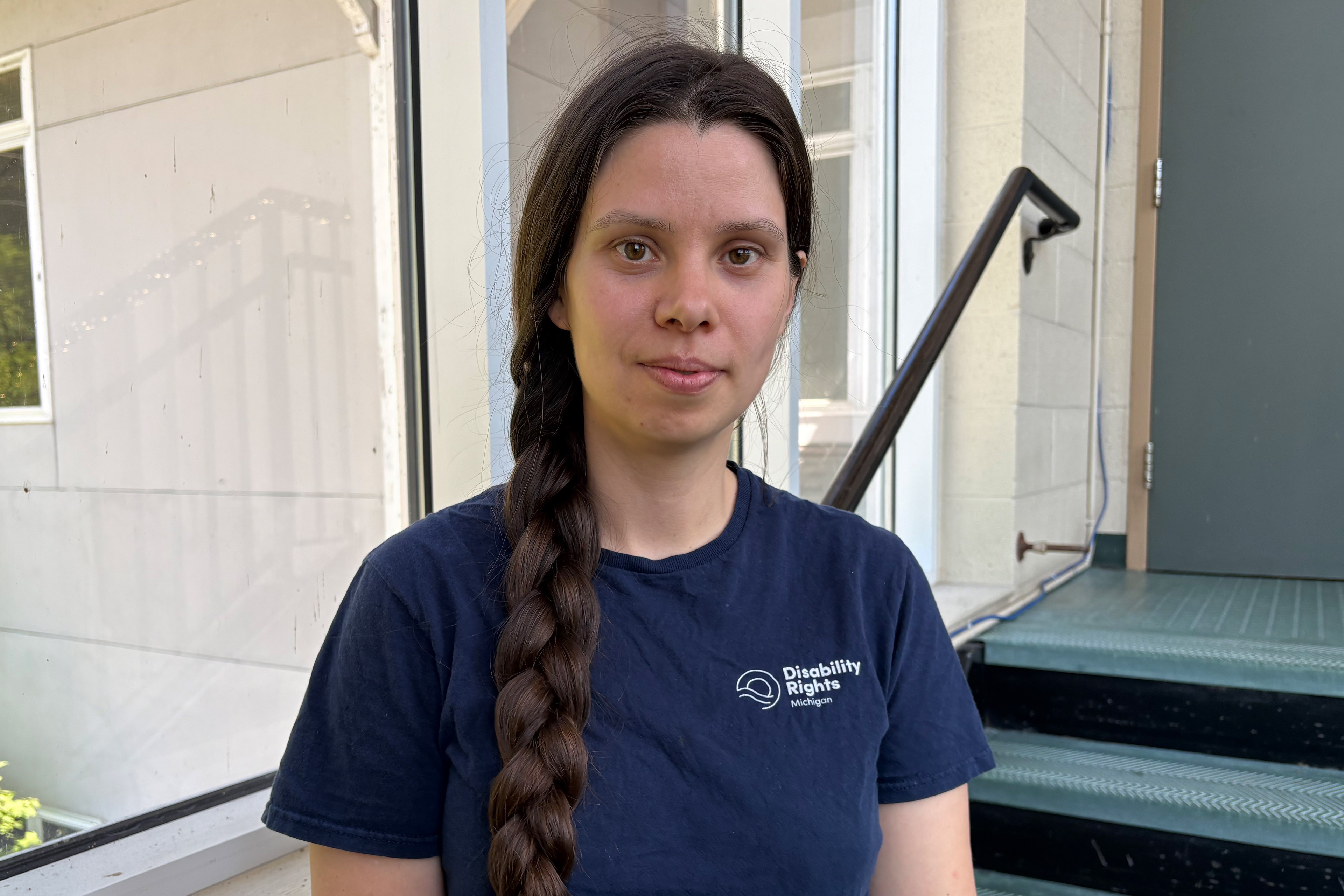 A woman stands in a stairwell. She wears a shirt that says "Disability Rights Michigan"