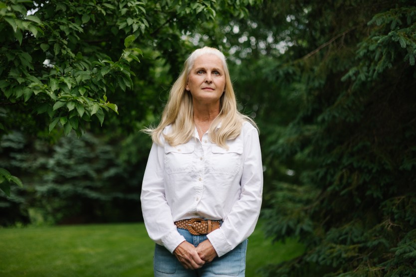 A woman wearing a white button-up shirt stands for a portrait amidst trees