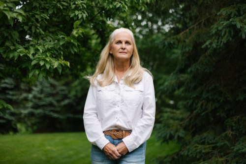 A woman wearing a white button-up shirt stands for a portrait amidst trees