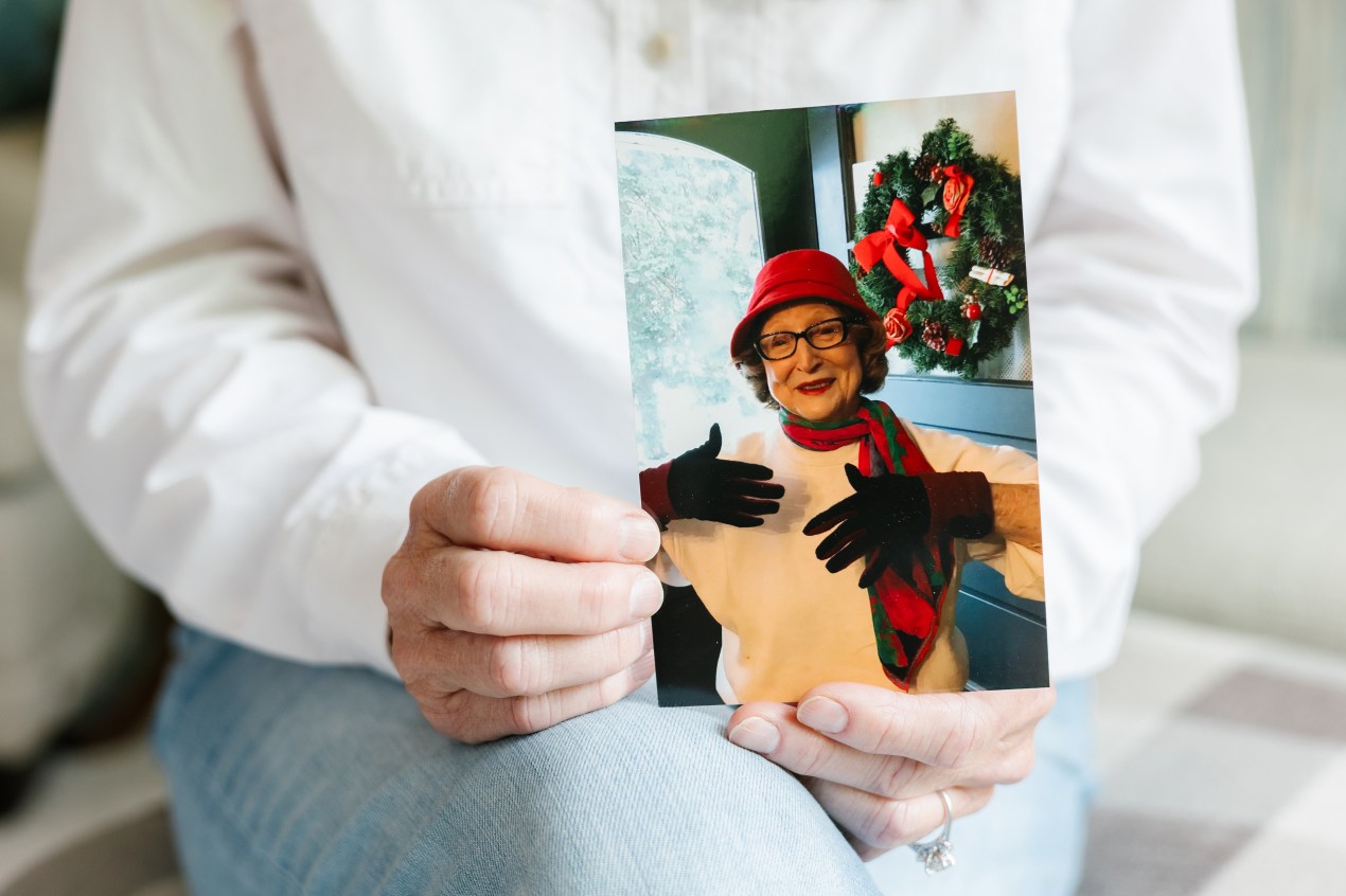 A woman wearing a white shirt holds a photo of a woman wearing black gloves, a red hat and a red and green scarf