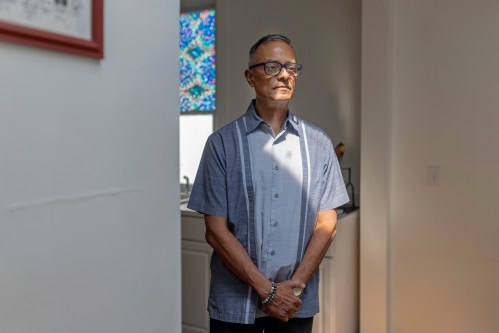 A man stands in the entryway to his kitchen at home.